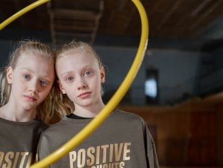 Twin girls in sportswear indoors with a hula hoop expressing positivity. Perfect for family and sports themes.